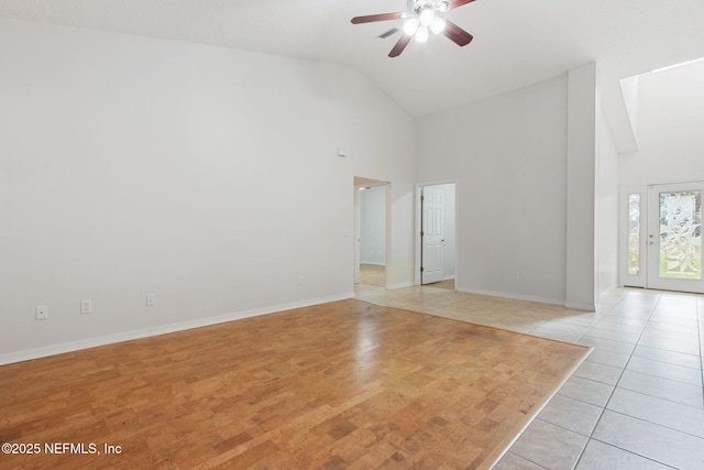 empty room with a ceiling fan, high vaulted ceiling, baseboards, and light tile patterned floors