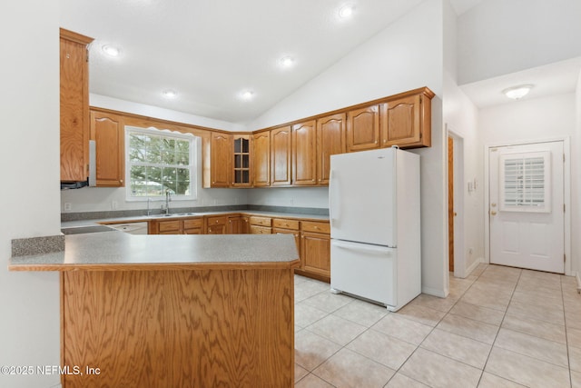 kitchen featuring light tile patterned floors, a peninsula, white appliances, a sink, and vaulted ceiling