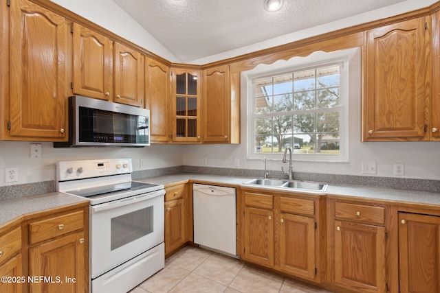 kitchen featuring brown cabinetry, lofted ceiling, white appliances, and a sink