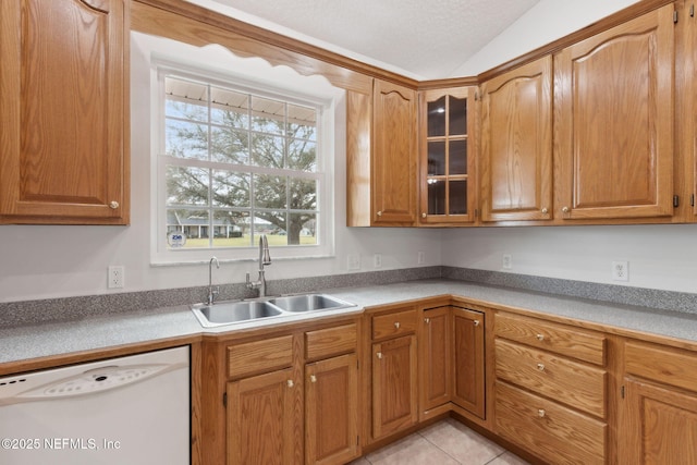 kitchen with light tile patterned flooring, white dishwasher, a sink, brown cabinets, and glass insert cabinets