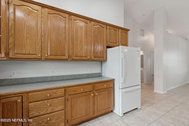 kitchen featuring brown cabinetry, freestanding refrigerator, light tile patterned flooring, and visible vents