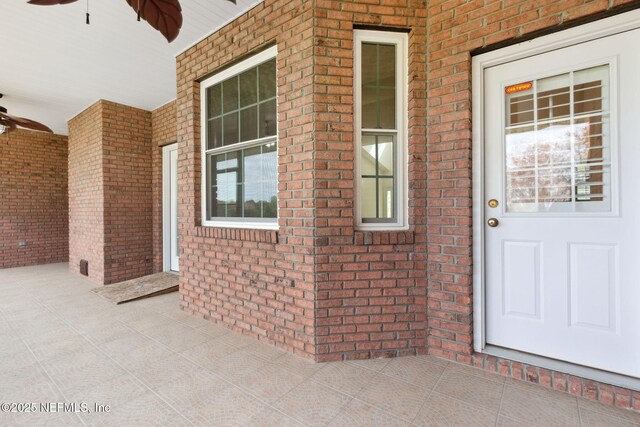 doorway to property featuring a porch, a ceiling fan, and brick siding