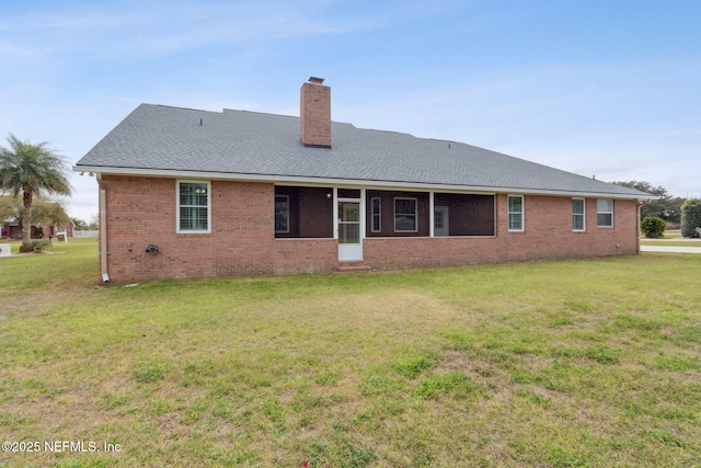 back of house with a yard, brick siding, a chimney, and roof with shingles