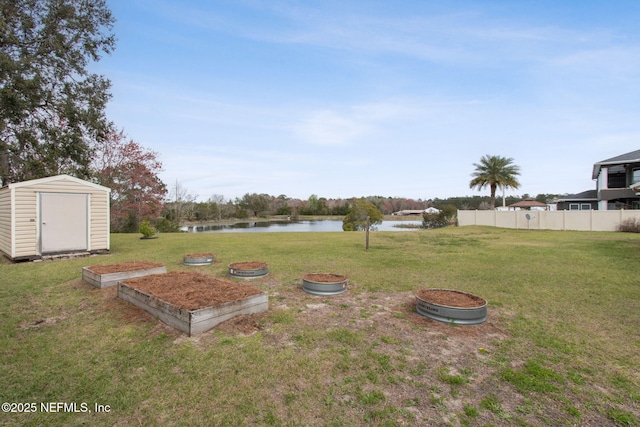 view of yard featuring an outbuilding, a water view, fence, a garden, and a storage unit