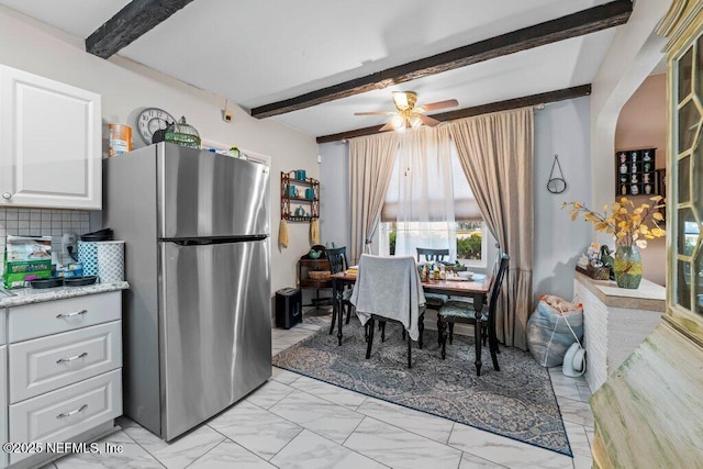 interior space featuring beamed ceiling, marble finish floor, white cabinets, and freestanding refrigerator