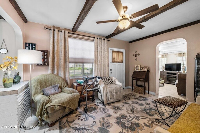 living room featuring beam ceiling, a ceiling fan, arched walkways, light tile patterned floors, and baseboards