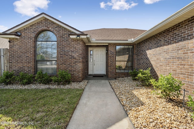 doorway to property featuring brick siding and roof with shingles