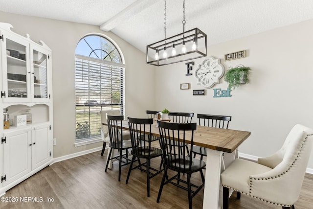 dining area featuring wood finished floors, baseboards, vaulted ceiling with beams, a textured ceiling, and a chandelier