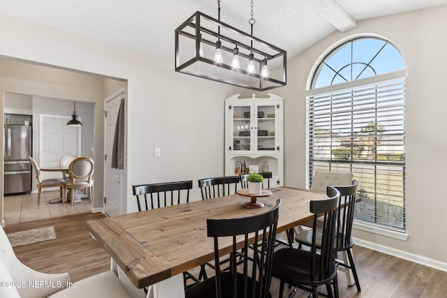 dining space featuring lofted ceiling with beams, wood finished floors, baseboards, and a textured ceiling