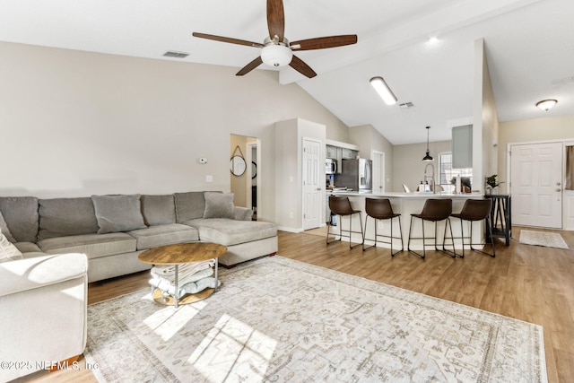 living area with visible vents, ceiling fan, vaulted ceiling, and light wood-style flooring