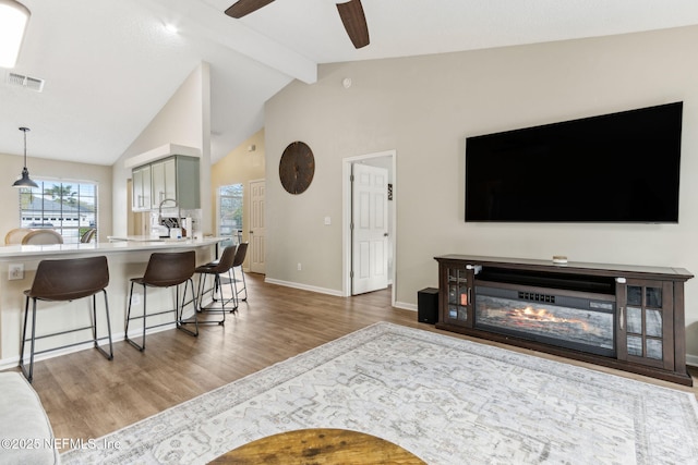 living room featuring wood finished floors, a ceiling fan, visible vents, baseboards, and beamed ceiling