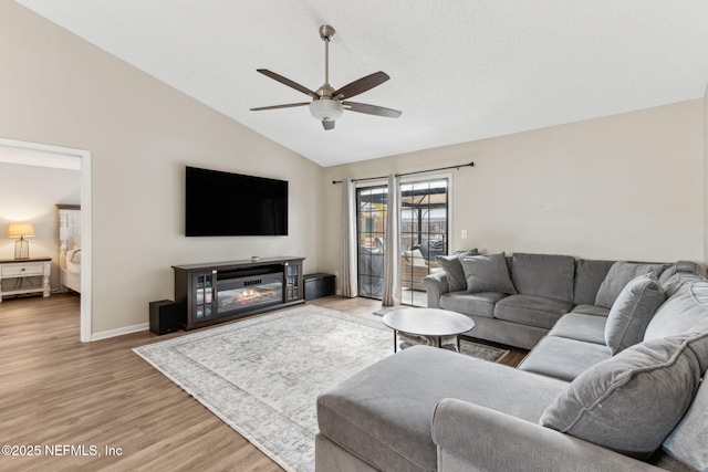 living room with baseboards, light wood finished floors, ceiling fan, vaulted ceiling, and a glass covered fireplace