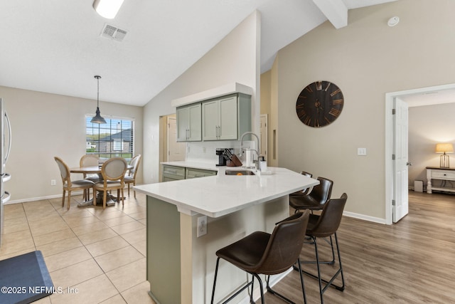 kitchen featuring visible vents, a peninsula, lofted ceiling with beams, a sink, and a kitchen breakfast bar