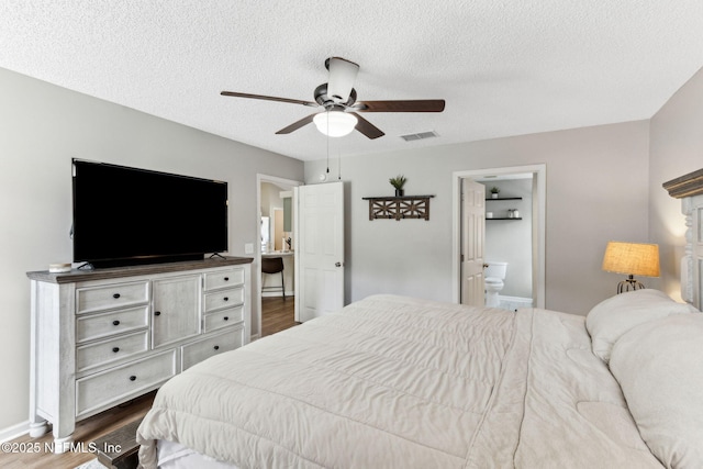 bedroom with dark wood finished floors, visible vents, a textured ceiling, and ensuite bathroom