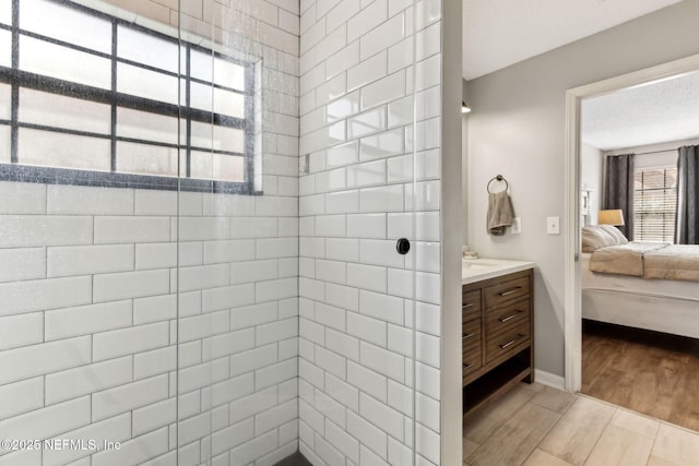 ensuite bathroom featuring connected bathroom, baseboards, tiled shower, wood finished floors, and vanity