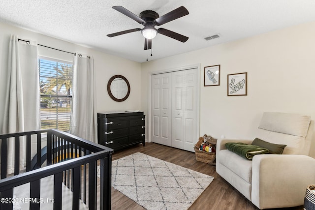 bedroom featuring visible vents, dark wood finished floors, ceiling fan, a closet, and a textured ceiling