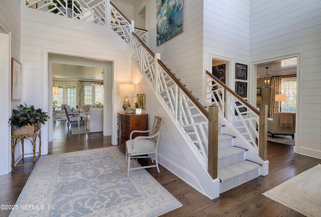 staircase featuring a high ceiling, an inviting chandelier, wood finished floors, and wood walls