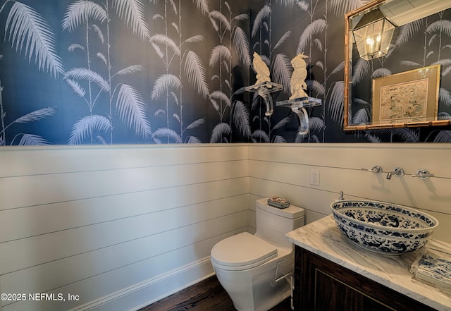 half bathroom featuring wallpapered walls, vanity, toilet, and wood finished floors