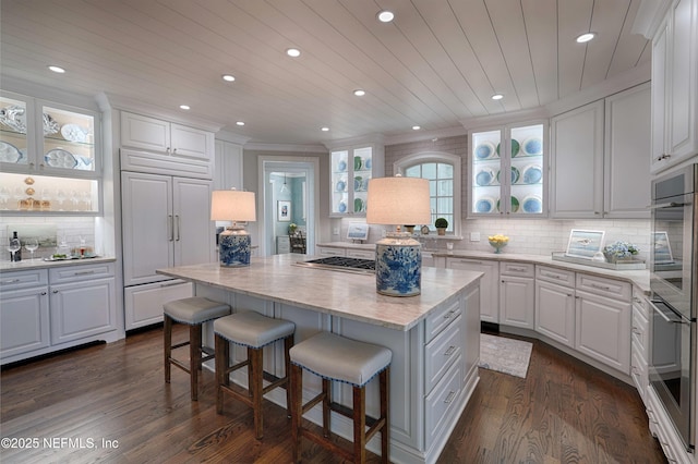 kitchen featuring a breakfast bar, stainless steel appliances, glass insert cabinets, white cabinetry, and a center island