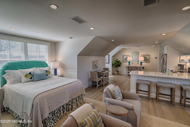 bedroom with visible vents, light wood-style flooring, freestanding refrigerator, and lofted ceiling