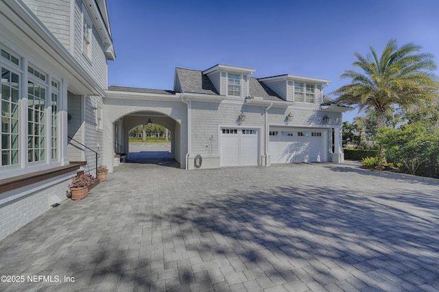 view of side of home with decorative driveway, roof with shingles, and an attached garage