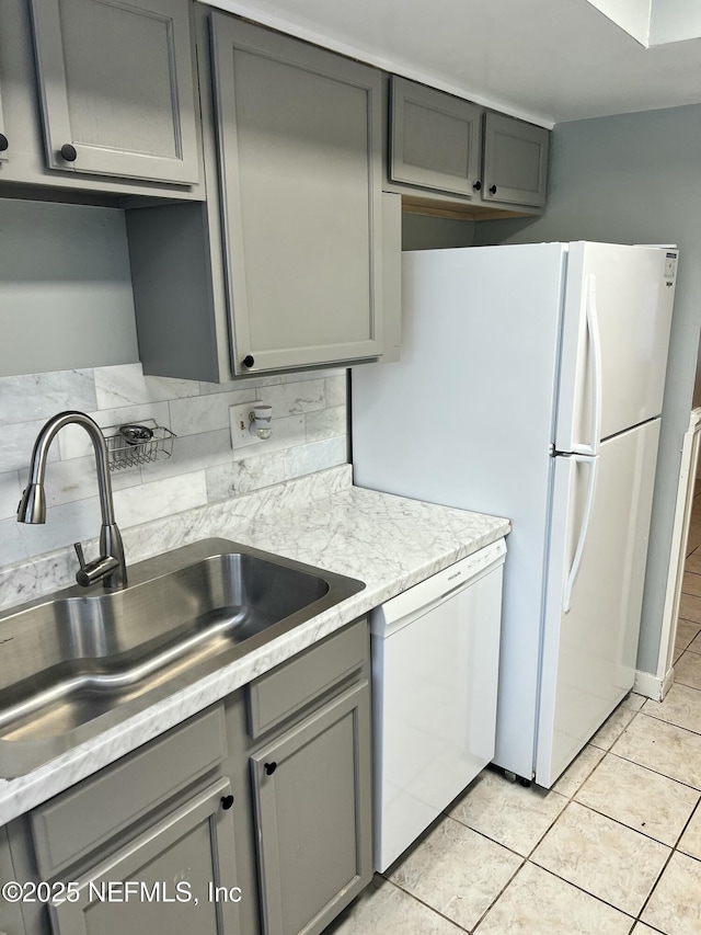 kitchen featuring gray cabinetry, white appliances, a sink, light countertops, and backsplash