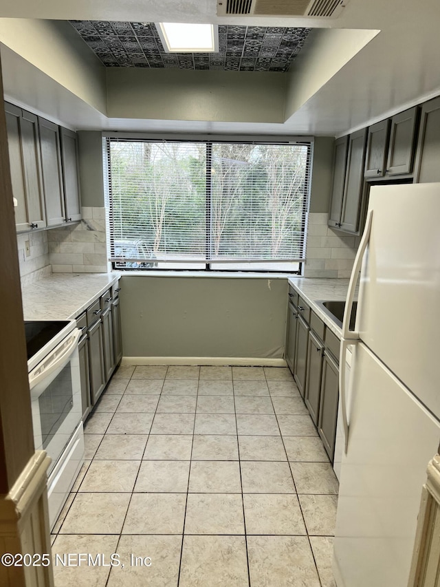 kitchen featuring plenty of natural light, white appliances, light tile patterned flooring, and backsplash