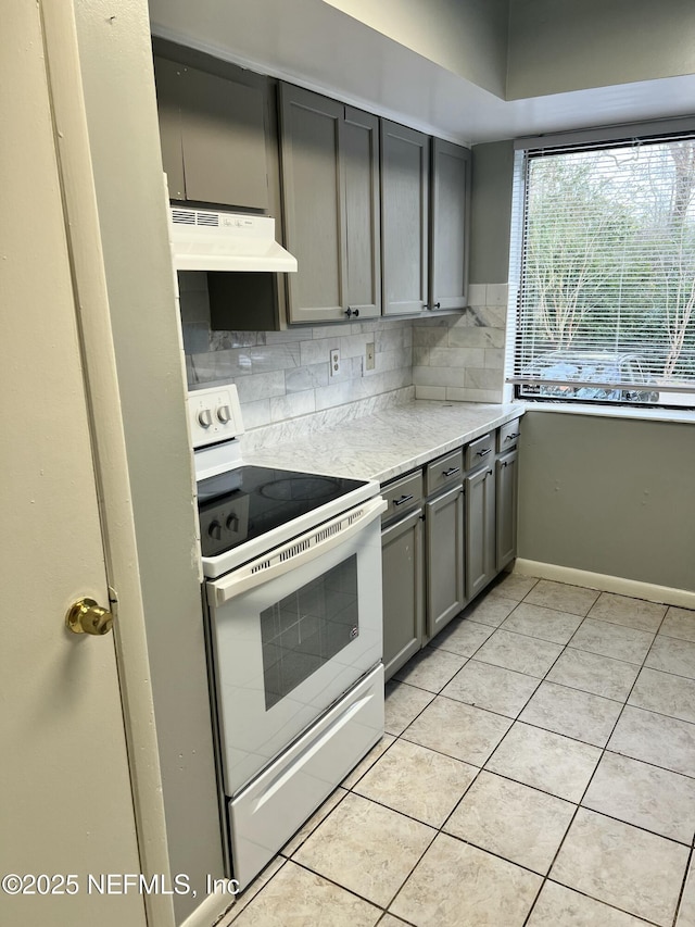 kitchen with gray cabinetry, under cabinet range hood, white electric range, light countertops, and decorative backsplash