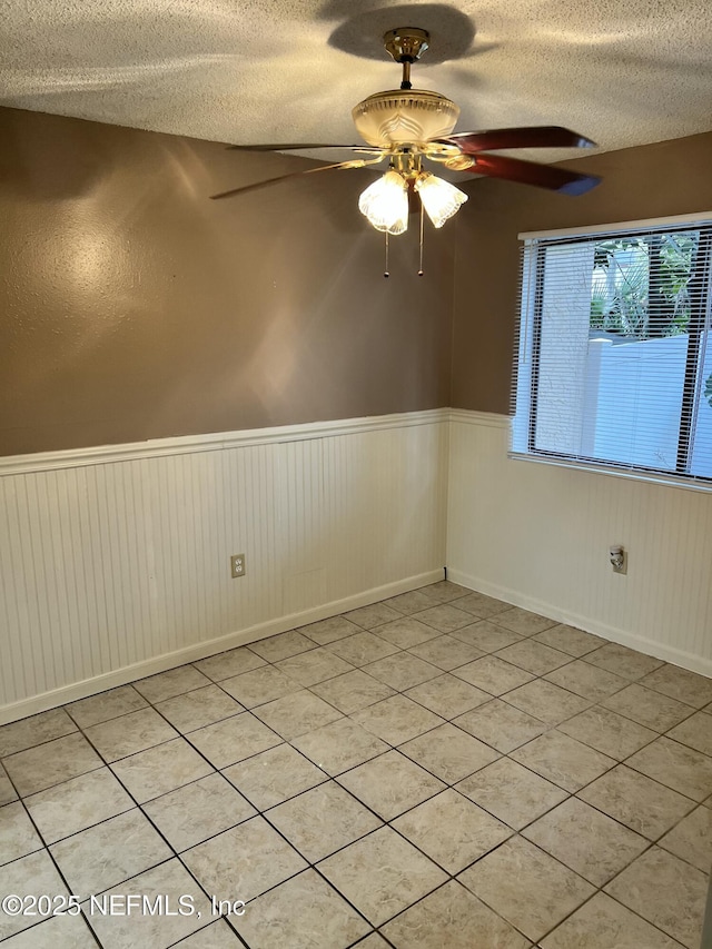 spare room with a wainscoted wall, ceiling fan, and a textured ceiling