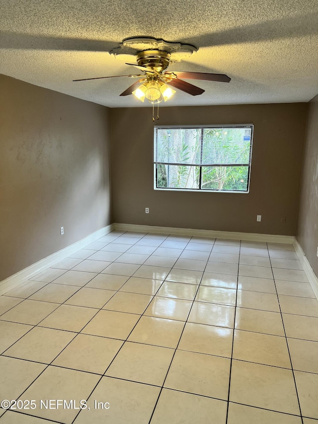 empty room with light tile patterned floors, a textured ceiling, a ceiling fan, and baseboards