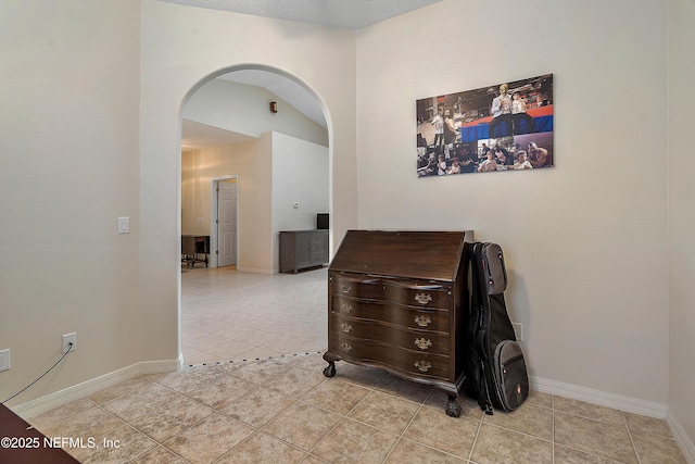 hall featuring light tile patterned floors, baseboards, and arched walkways