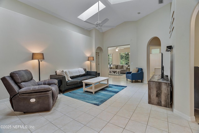 living room with high vaulted ceiling, arched walkways, a skylight, and light tile patterned floors