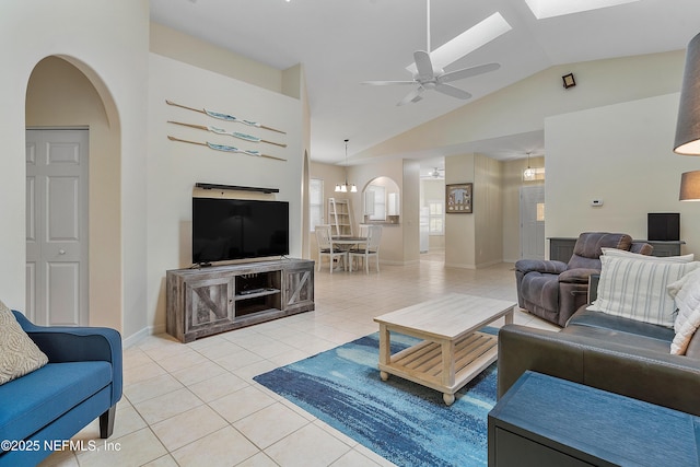 living area with arched walkways, light tile patterned flooring, a ceiling fan, baseboards, and vaulted ceiling