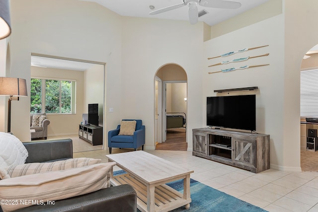 living room featuring a ceiling fan, arched walkways, a towering ceiling, and light tile patterned floors