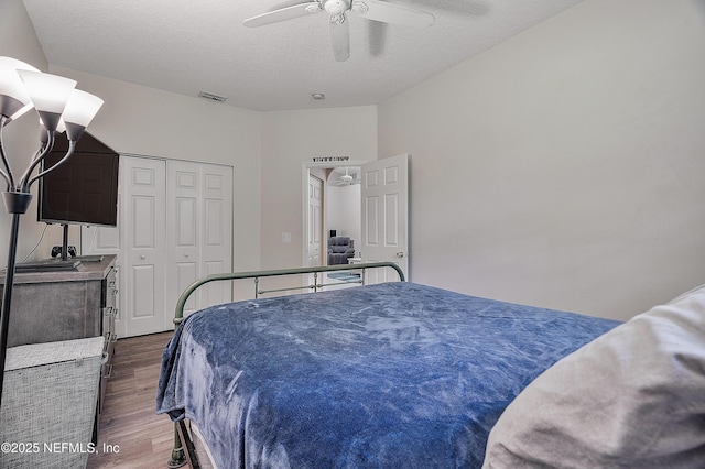 bedroom with a textured ceiling, wood finished floors, visible vents, a ceiling fan, and a closet