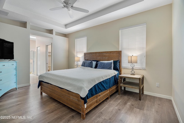 bedroom featuring a raised ceiling, light wood-style flooring, and baseboards