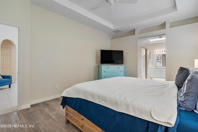 bedroom featuring baseboards, arched walkways, a raised ceiling, and wood finished floors