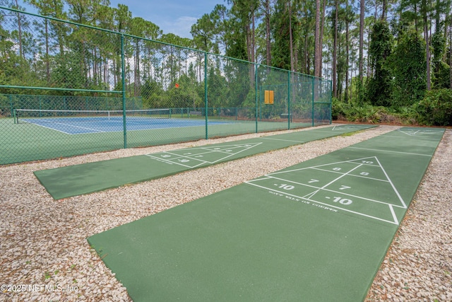 view of property's community featuring a tennis court, shuffleboard, and fence