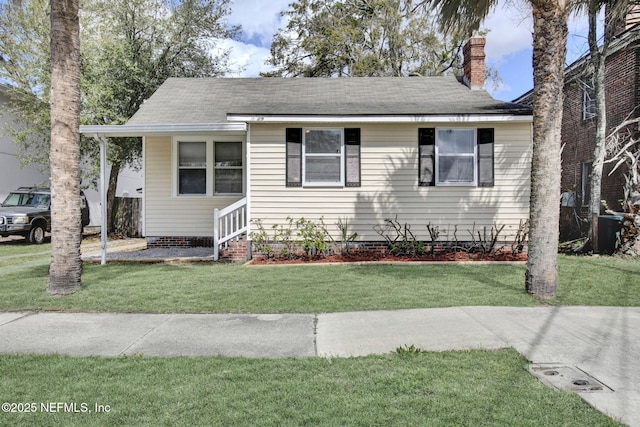 bungalow-style house with entry steps, a shingled roof, a chimney, and a front yard