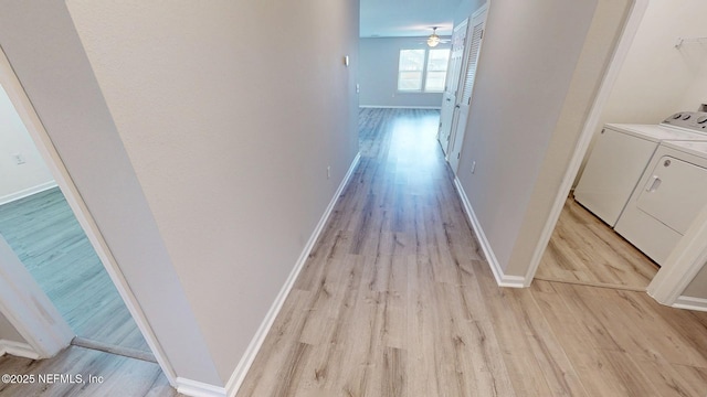 hall with light wood-style flooring, baseboards, and washing machine and clothes dryer