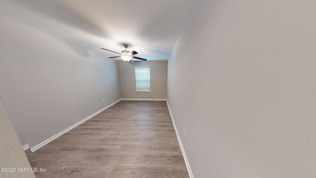 empty room with a textured ceiling, baseboards, a ceiling fan, and light wood-style floors