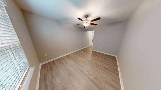 spare room featuring light wood-type flooring, a ceiling fan, and baseboards