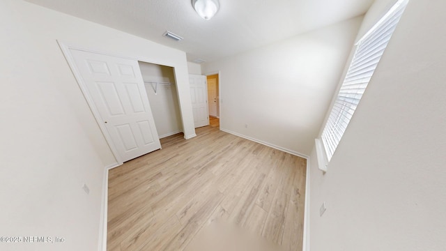 unfurnished bedroom with light wood-style flooring, a closet, visible vents, and baseboards