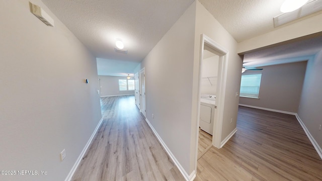 hallway with visible vents, a textured ceiling, washer / dryer, and light wood-style floors