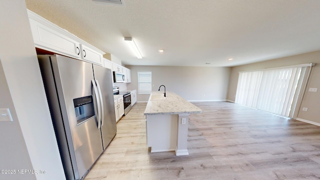 kitchen featuring light wood finished floors, appliances with stainless steel finishes, a kitchen island with sink, white cabinets, and a textured ceiling