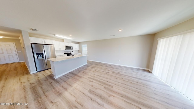 kitchen featuring a center island with sink, light wood finished floors, stainless steel appliances, visible vents, and white cabinetry