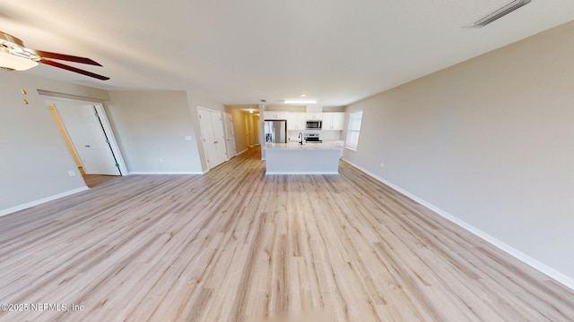 unfurnished living room featuring light wood-type flooring, a ceiling fan, and baseboards