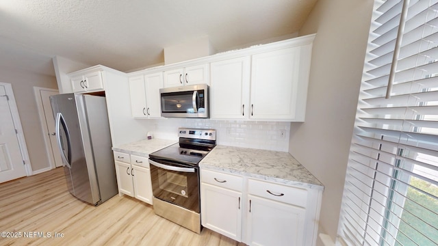 kitchen featuring light wood-style flooring, stainless steel appliances, white cabinetry, decorative backsplash, and light stone countertops