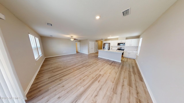 unfurnished living room with a ceiling fan, light wood-type flooring, visible vents, and baseboards