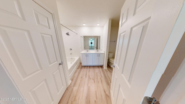 bathroom featuring a textured ceiling, toilet, wood finished floors, vanity, and tub / shower combination